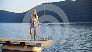 Happy girl teenager dancing on pier on green hills and yacht landscape. Cheerful young girl dancing on sea pier on green