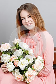 Happy girl teenager in dress sits on couch with flowers