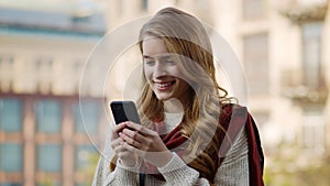 Happy girl texting smartphone outdoors. Cheerful woman using phone on street.