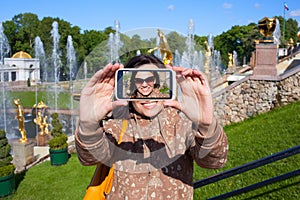 Happy girl tourist shooting selfie in Peterhof in Saint Petersburg