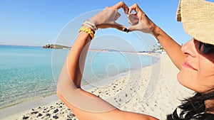 Happy girl tourist on sunny Nissi beach in Cyprus show Finger shaped heart shape sign. Hands of girl shape of heart. Summer dream