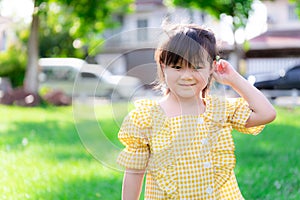 Happy girl tucked a flower from the grass to her ear. Cute kids play with nature in the white lawn in warm summer or spring sun.