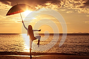 Happy girl with an umbrella jumping on the beach