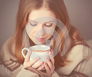 Happy girl is under a blanket and cup of coffee on winter morning at home