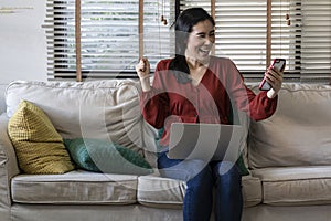 Happy girl using a laptop and smart phone. Happy young woman using phone, browsing mobile device app, playing game, on sofa.