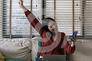 Happy girl using a laptop and smart phone. Happy young woman using phone, browsing mobile device app, playing game, on sofa.
