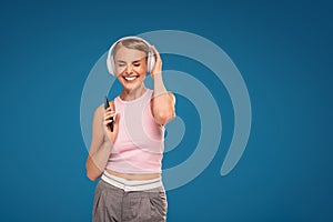 Happy girl using mobile phone listening music with headphones and singing a song loud. Photo of fashionable woman with beautiful