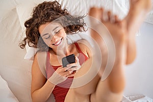 Happy girl using phone while lying on bed in the morning
