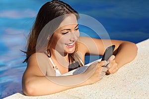 Happy girl using a smart phone in a swimming pool in summer vacations