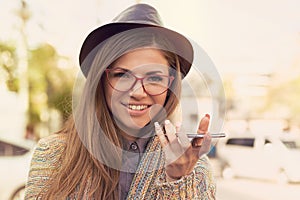 Happy girl using a smart phone voice recognition function on line walking on a street