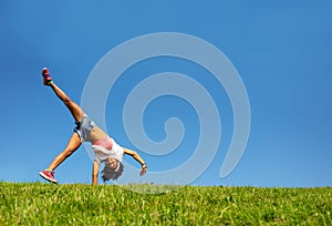 Happy girl walk on hands over blue sky and grass