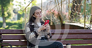Happy girl walking listening to music with smart phone and earbuds in a park. Attractive woman browsing on mobile phone