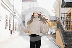 A happy girl in a warm sweater and hat runs through the autumn city. She develops hair in the wind