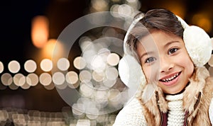 Happy girl wearing earmuffs over christmas lights