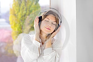 Happy girl wearing headphones. Relaxed young woman enjoying calm music in wireless earphones at home