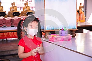 Happy girl went to make merit at temple on New Year Day. Cute kid wearing 3D shaped mask. Child wear red dress. Sweet smile