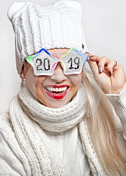 Happy girl in a white hat and scarf, wearing funny glasses with the inscription `2019`.