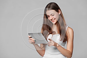 Happy girl in white shirt using tablet. Smiling woman with tablet pc, isolated on grey background