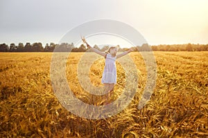 A happy girl in a white sundress jumps on a field of ripe wheat in the rays of the setting sun. Wheat ear. Ears of rye. Selective
