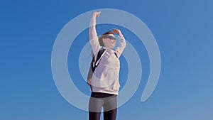 Happy girl winner jumps in victory pose with raising hands blue sky background.