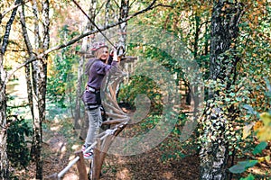 Happy girl, woman, climbing gear in an adventure, rope road, insurance, attraction, amusement park, active recreation, autumn