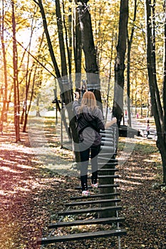 Happy girl, woman, climbing gear in an adventure, rope road, insurance, attraction, amusement park, active recreation, autumn