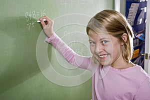 Happy girl writing math on blackboard in class