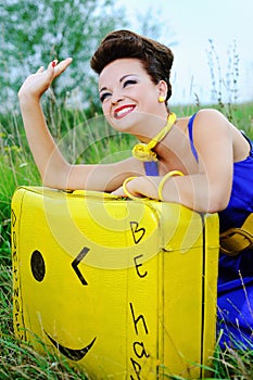 Happy girl with a yellow suitcase waving goodbye