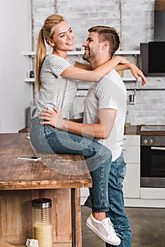 happy girlfriend sitting on kitchen counter and cuddling boyfriend
