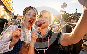 Happy girlfriends eating candy apple on a Bavarian fair or oktoberfest or duld in national costume or Dirndl in germany