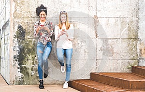 Happy girls best friends having fun outdoors with mobile smart phone - Friendship concept with millenial girlfriends