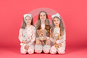 Happy girls children holding teddy bears sitting together in homewear pink background, girlhood photo