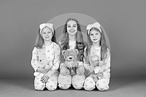 Happy girls children holding teddy bears sitting together in homewear pink background, girlhood photo