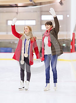 Happy girls friends waving hands on skating rink