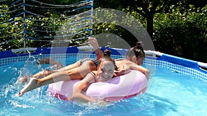 Happy girls have fun floating together on swim ring in outdoor swimming pool, summer