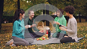 Happy girls are having picnic in park sitting on yoga mats and eating after outdoor practice in autumn, girls are