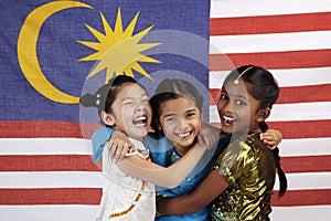 Happy girls hugging each other with Malaysian flag in the background. Conceptual image photo
