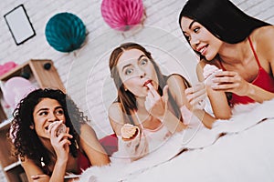 Happy Girls Lying on White Bed Eating Cupcakes.