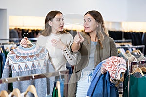 Happy girls pointing finger at new clothes in clothing store