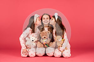 Happy girls in pyjamas kissing elder sister sitting together with teddy bears, sisterly love.