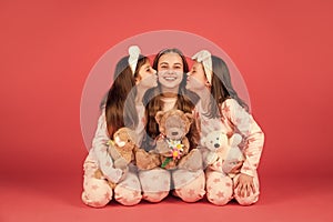 Happy girls in pyjamas kissing elder sister sitting together with teddy bears, sisterly love.