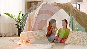 Happy girls reading book in kids tent at home