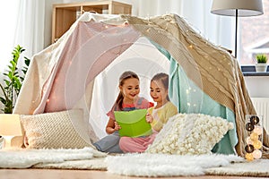 Happy girls reading book in kids tent at home