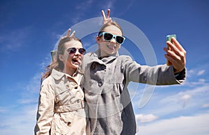 Happy girls with smartphone taking selfie outdoors