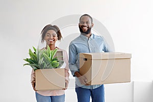 Happy glad millennial african american male and female carry cardboard boxes with plant and relocate to new apartment