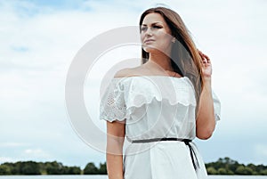 Happy glamorous beautiful girl in a white light dress on a background of a sky