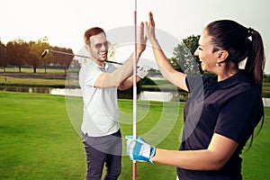 Happy golf player couple giving high five while standing on field