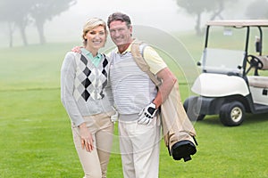 Happy golfing couple with golf buggy behind