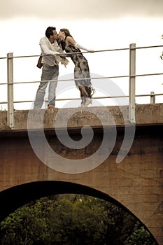 Happy good looking couple leaning on bridge railling kissing