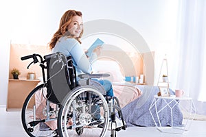 Happy good-looking smiling paralyzed woman holding a book